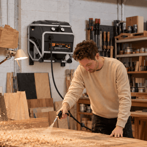 Wall-mounted FlexReel air compressor blowing sawdust off a workbench